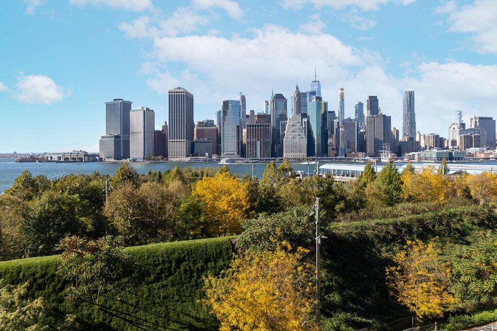 A view of one of the sound berms in autumn at Brooklyn Bridge Park with the East River and lower Manhattan in the distance. 