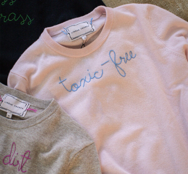 A Lingua Franca x Perfect Earth Project collaboration featuring a pastel pink cashmere sweater with periwinkle blue embroidery that says 'Toxic-free.'