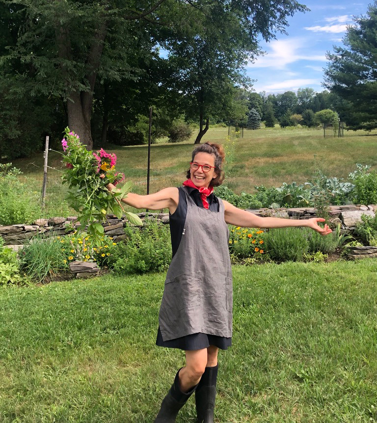 Dana Cowin holding flowers wearing a taupe apron in a garden.
